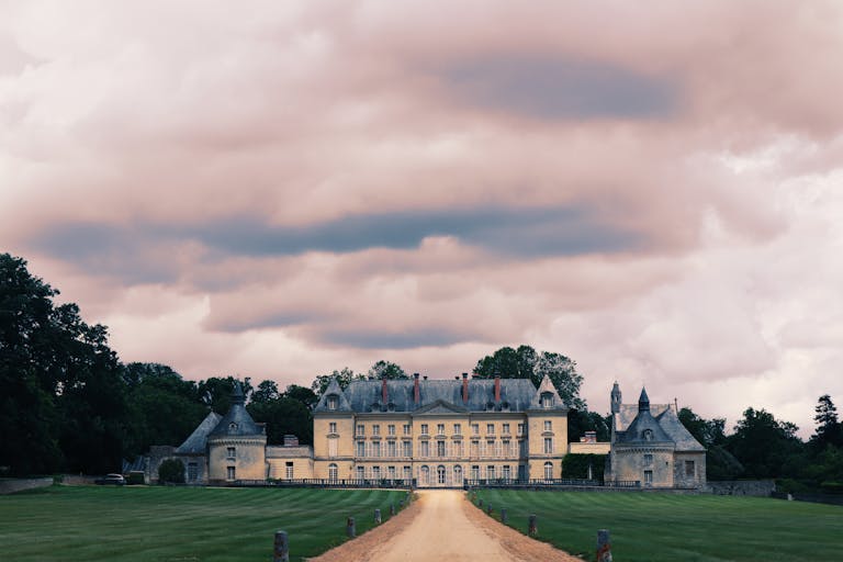 Impressive French chateau surrounded by lush greenery under a moody, cloudy sky.