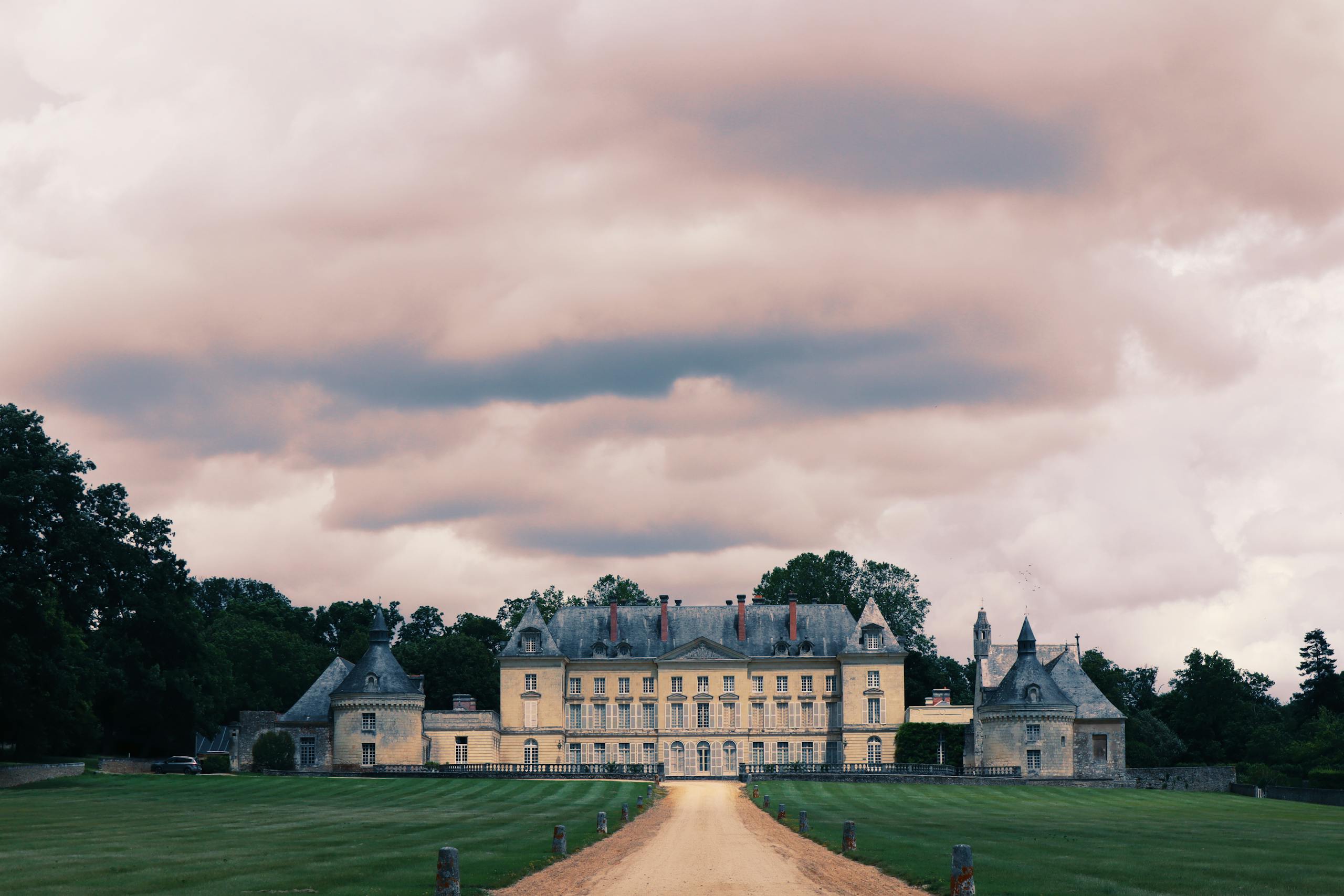 Impressive French chateau surrounded by lush greenery under a moody, cloudy sky.