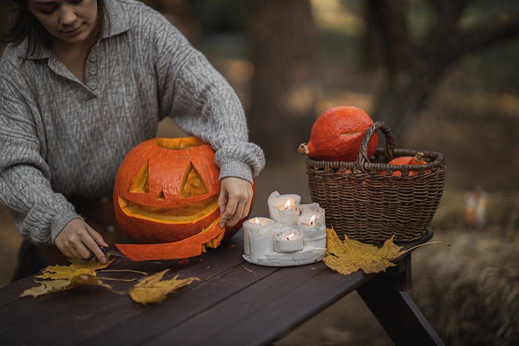 Woman carving a pumpkin outdoors with candles and autumn leaves. Perfect for Halloween or Thanksgiving.
