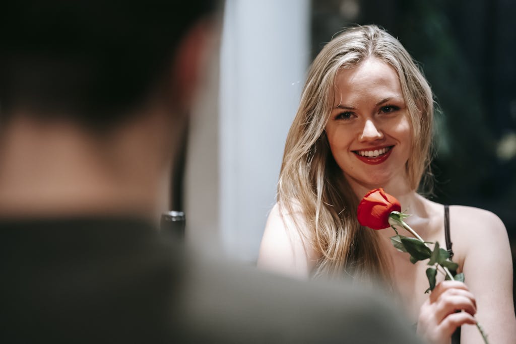 Smiling woman with a red rose in a romantic indoor setting, perfect for Valentine's celebration.
