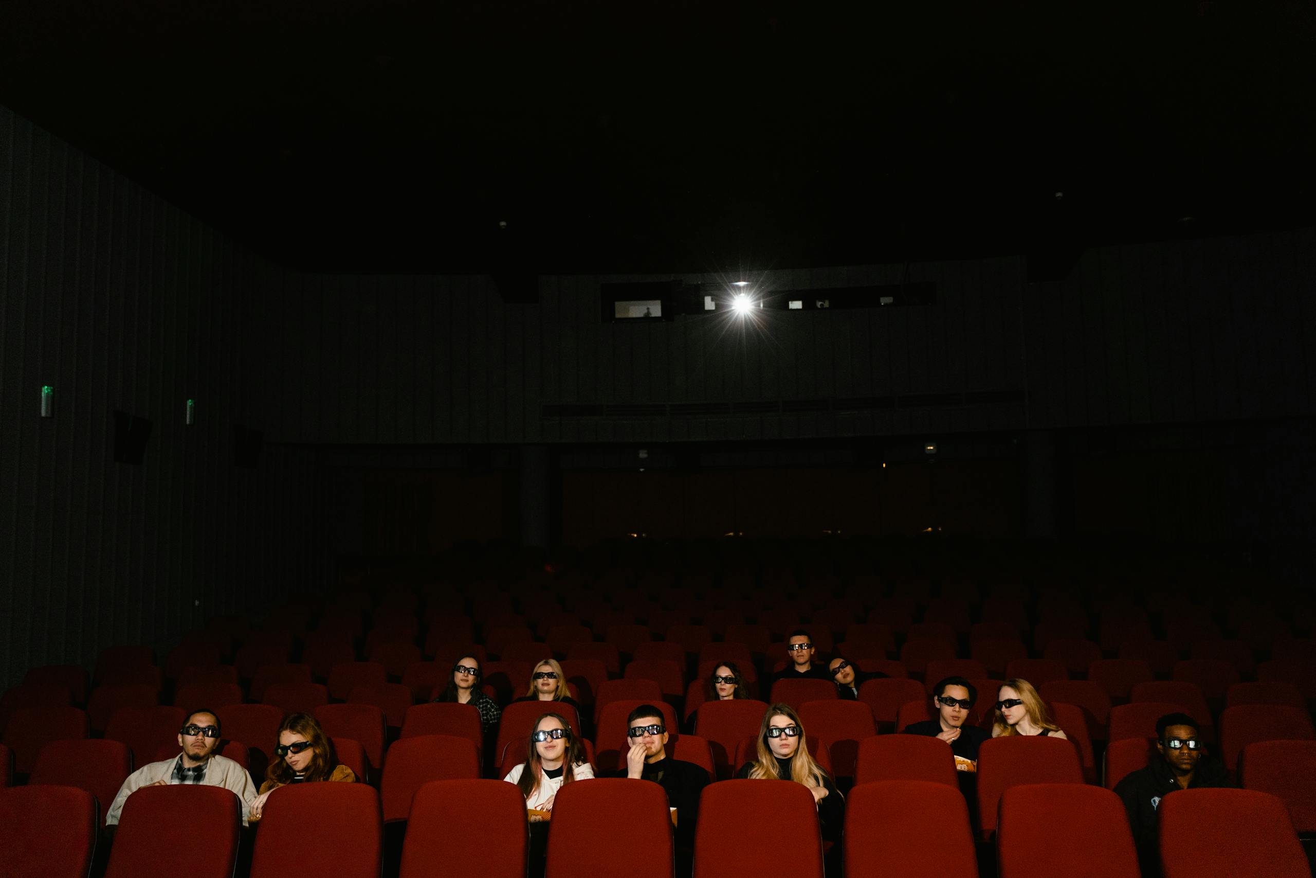 A group of people in a cinema watching a 3D movie wearing glasses, sitting in a dark theater.