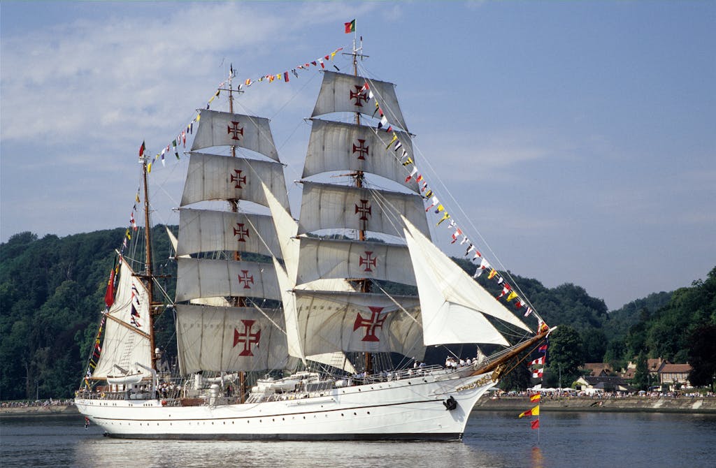 A grand tall ship with white sails and colorful flags sailing in Rouen, France.