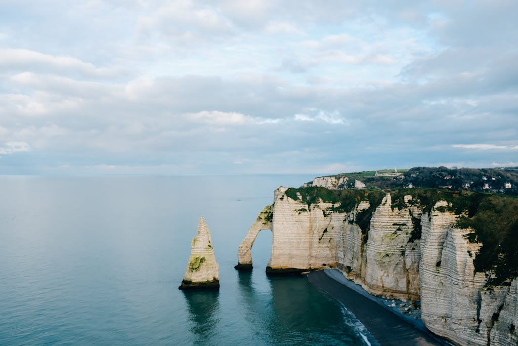 Rocky rough cliffs covered with fresh green moss and washed by peaceful water of vast ocean under cloudy sky