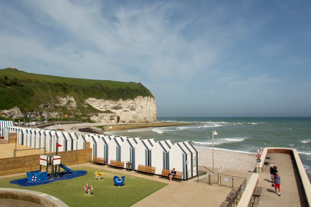Scenic view of Yport beach with beach huts, playground, and cliffs, Normandy, France.