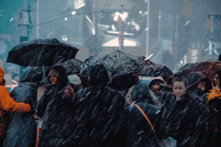 People with umbrellas navigate a busy urban street amid heavy snowfall, creating a wintery urban scene.