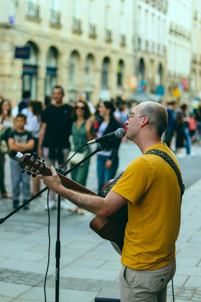 A street musician performing with a guitar and microphone on a busy street in Rennes, France.